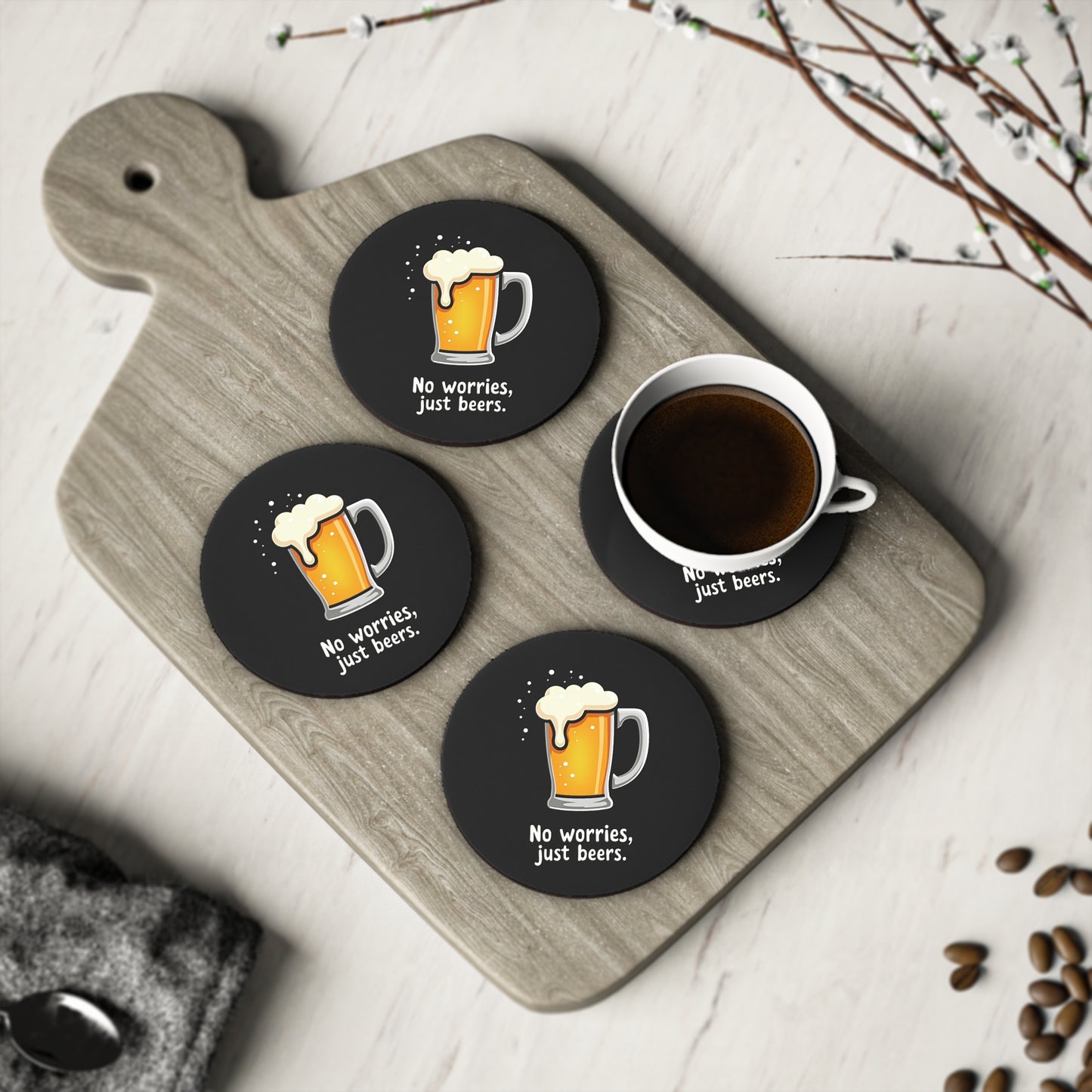 Set of 4 round black No Worries Coasters with beer mug print, styled on timber board with coffee cup