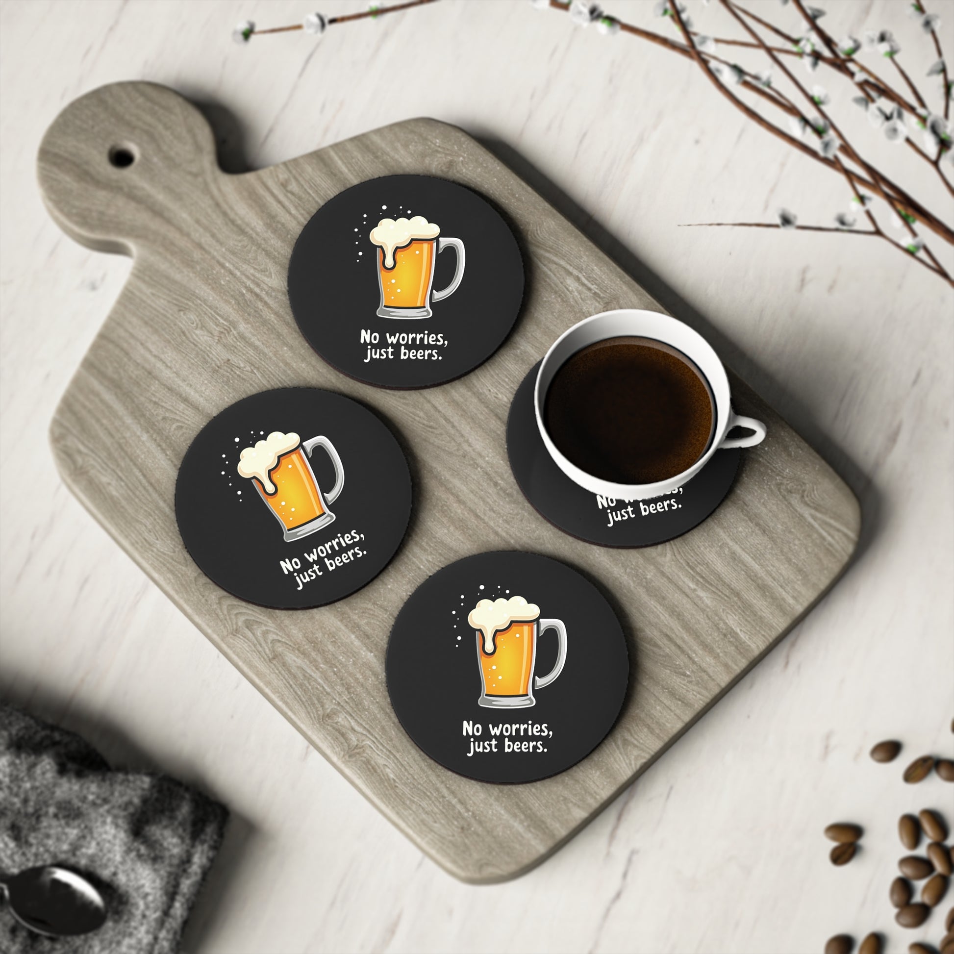 Set of 4 round black No Worries Coasters with beer mug print, styled on timber board with coffee cup