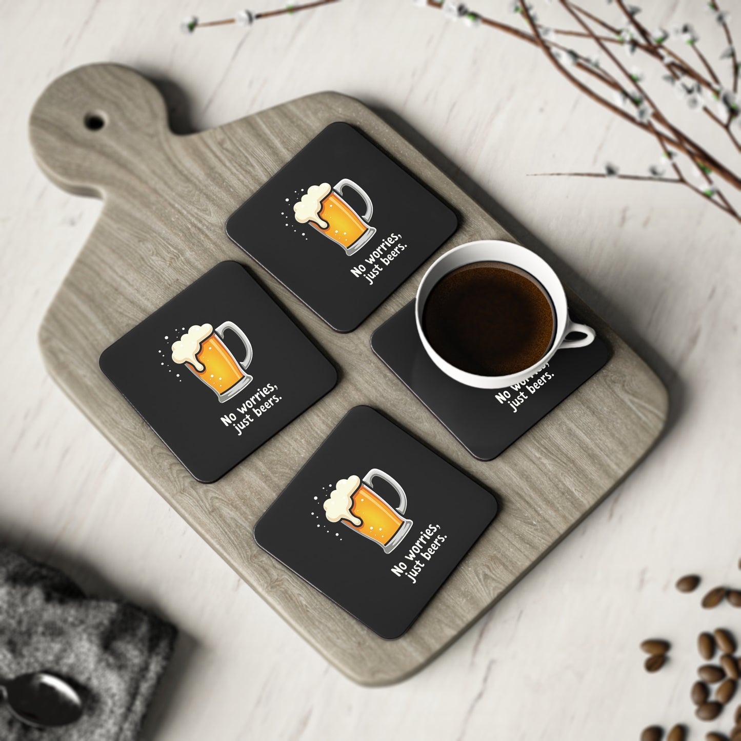 Set of 4 black No Worries Just Beers coasters with beer mug print, displayed on a wooden board with a coffee cup