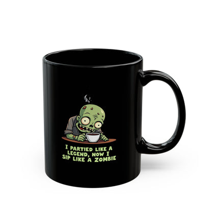 Black coffee mug with cartoon zombie sipping coffee and text 'I Partied Like a Legend, Now I Sip Like a Zombie'