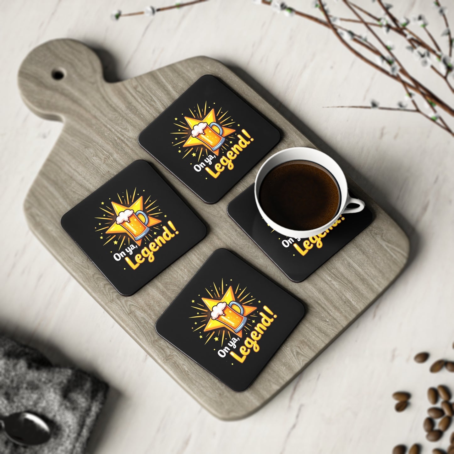 Set of 4 black "On ya, Legend!" coasters with beer mug design on wooden board, one holding a coffee cup
