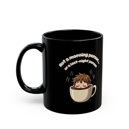 Black ceramic coffee mug with cartoon sleepy face in cup and "Not a morning person" funny text design