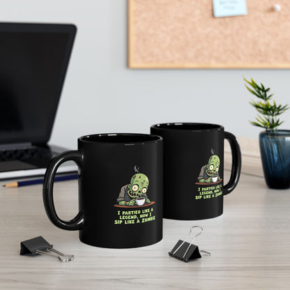 Black coffee mug with cartoon zombie and text 'I Partied Like a Legend, Now I Sip Like a Zombie'